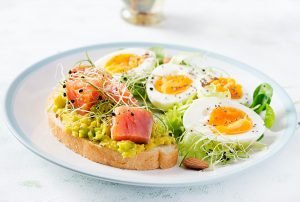 Healthy open sandwich on toast with avocado and salmon, boiled eggs, herbs