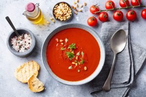 Tomato Soup with Fresh Herbs and Pine Nuts in a Bowl. Grey Stone Background. Top view.